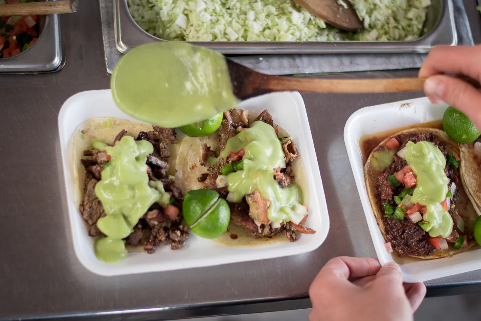 Two trays of Sonoran tacos with guacamole, lime, and salsa from Tacos Apson.